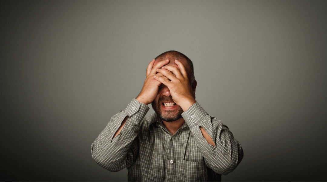 headshot of a person that has a frustrated expression with his hands over his eyes.
