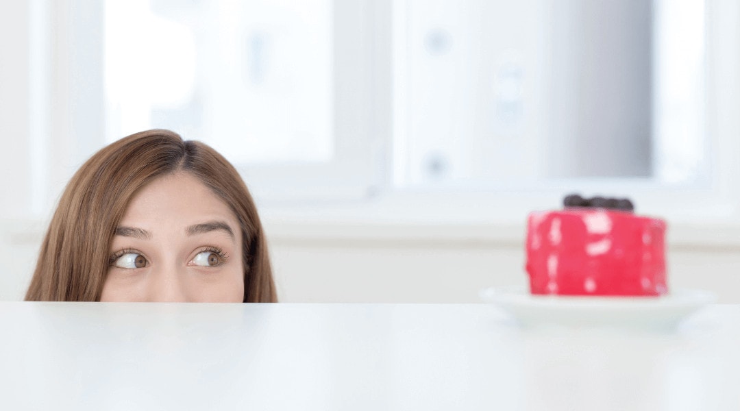 half a persons face peaking from behind a counter to look at a red cake