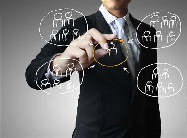 Man in suit drawing a diagram showing groups of people in circles pointing to one person in the middle