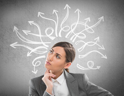 a headshot of a women in a suit with her fingers on her chin looking up thinking, with white arrows going in every direction from her head