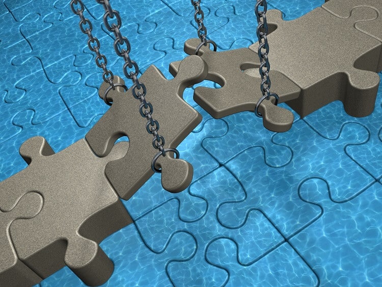 Grey puzzle bridge hangs over blue puzzle water and is lifted my chains