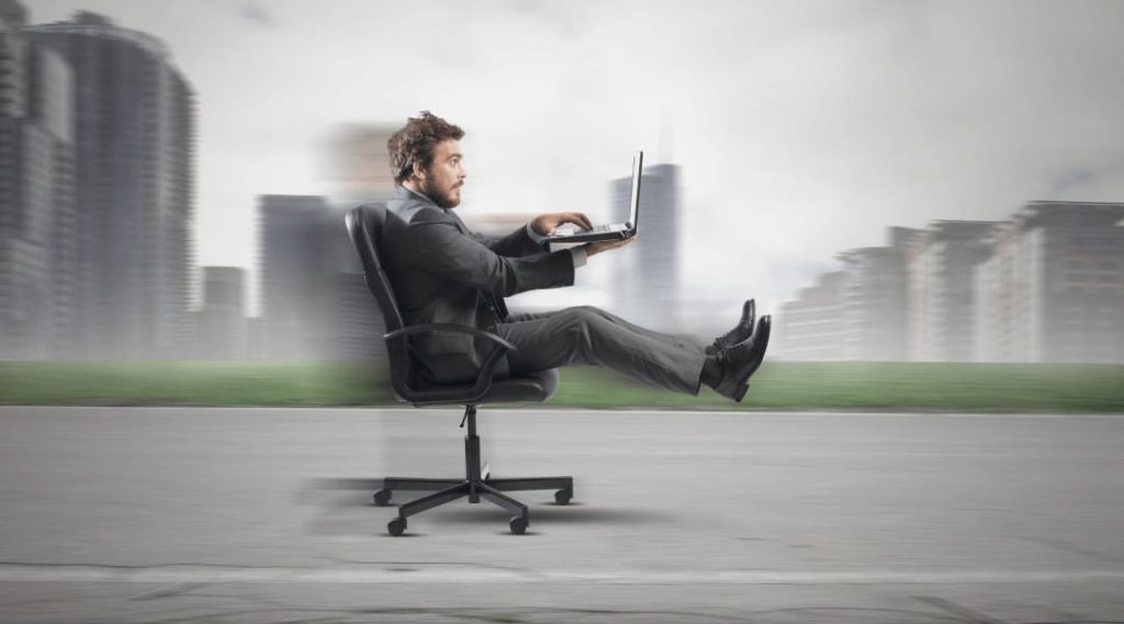 a person working on his laptop sitting in an office chair that is "driving" on the road