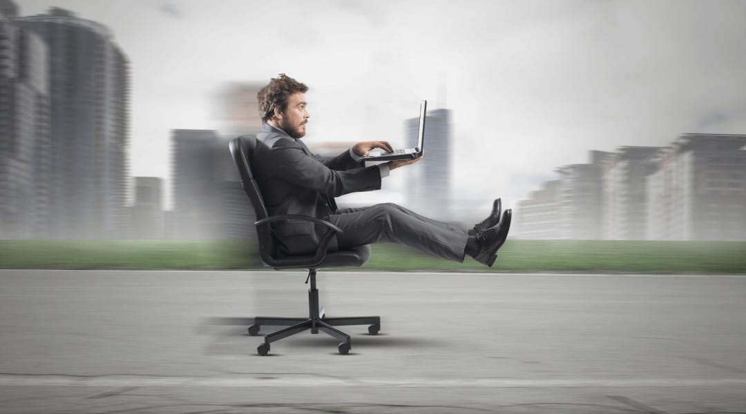 a person working on his laptop sitting in an office chair that is "driving" on the road