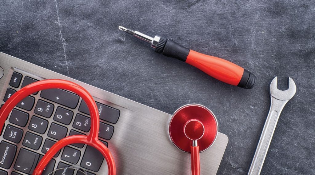a metal wrench and orange screw driver next to a red stethoscope on a grey laptop keyboard
