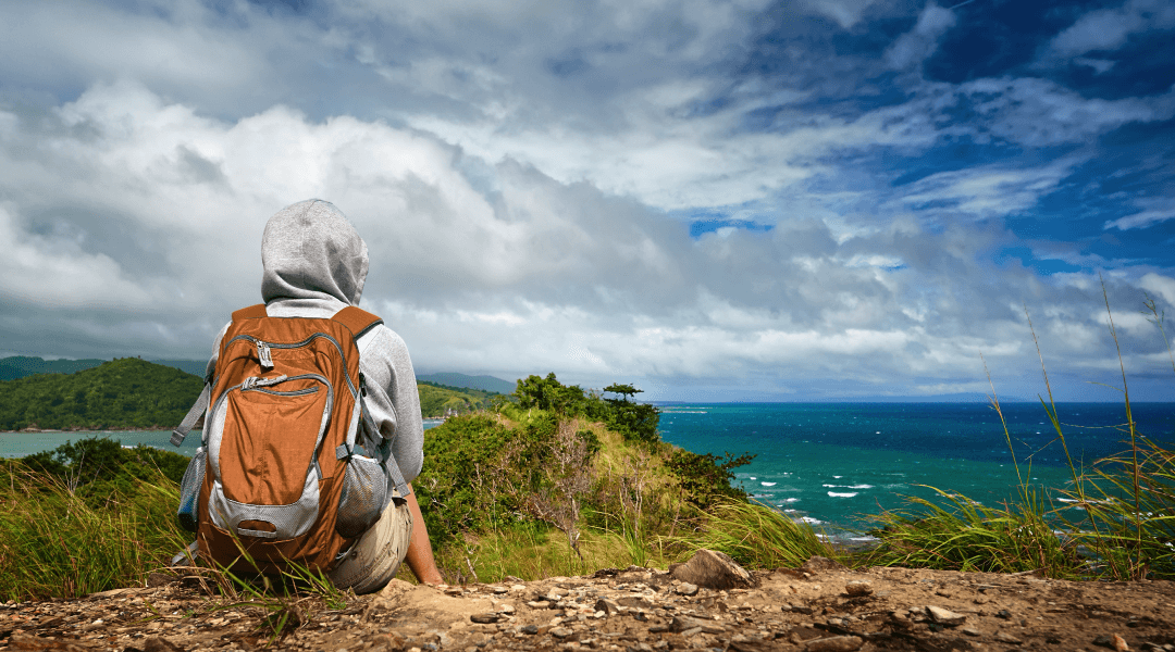 a person sitting on a cliff looking out to the ocean.