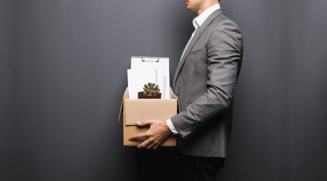 a professional individual holding a cardboard box filled with papers and a plant.