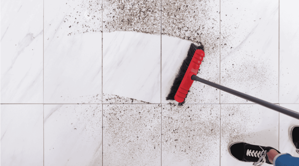 a person sweeping a dirty floor with a red broom.
