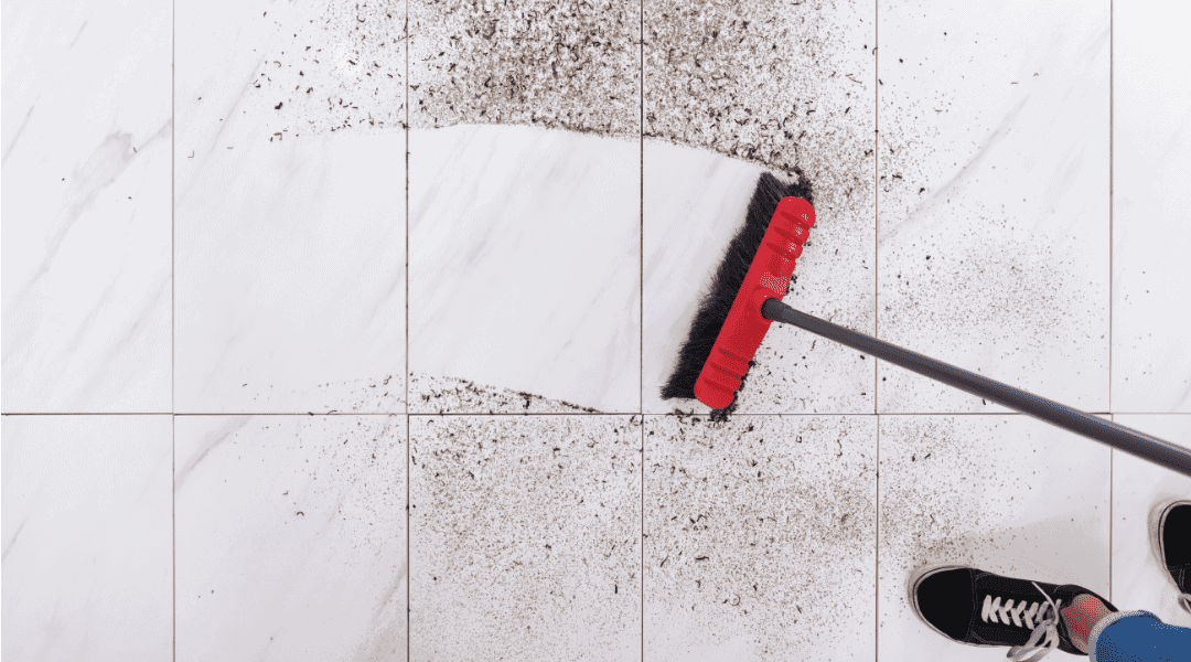 a person sweeping a dirty floor with a red broom.