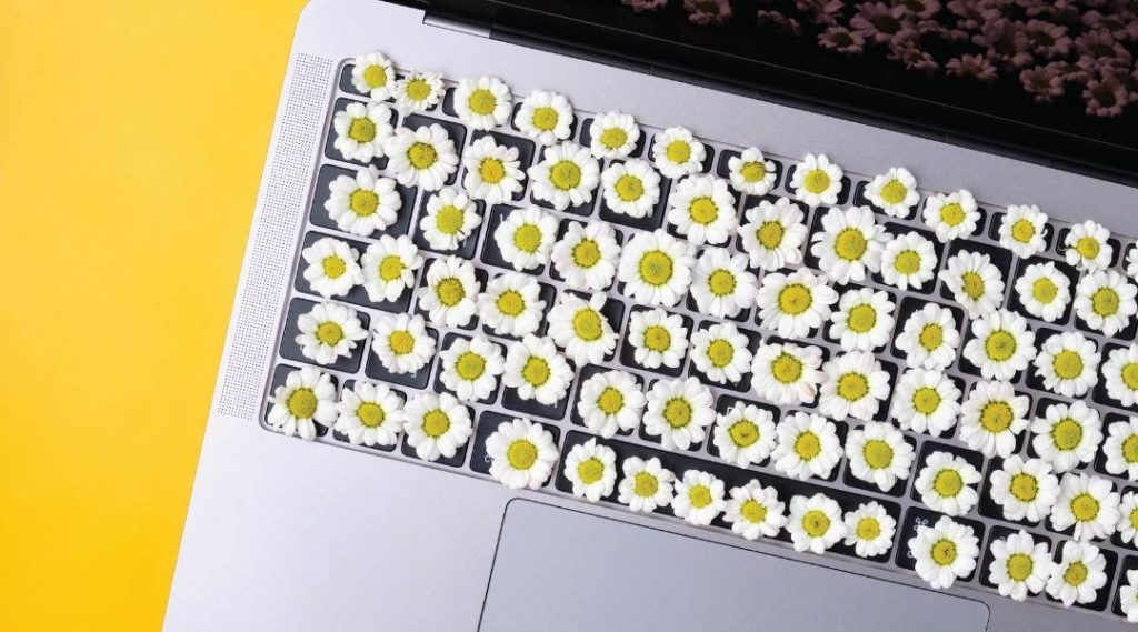 Laptop with flowers on keyboard over yellow background