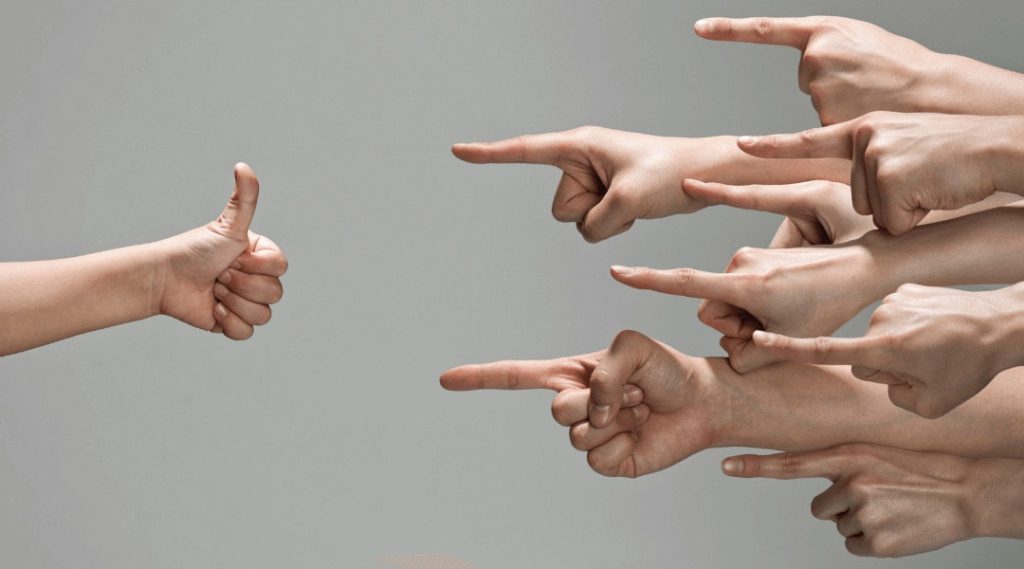 close up of eight peoples hands pointing fingers to one persons hand holding a thumbs up