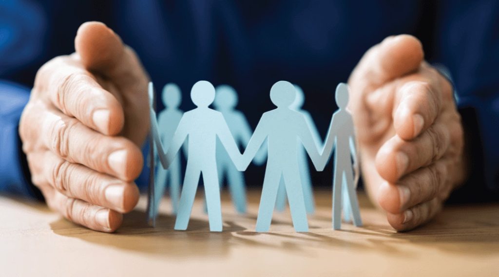 close up of a persons hands protecting a circle of blue paper cut out people.