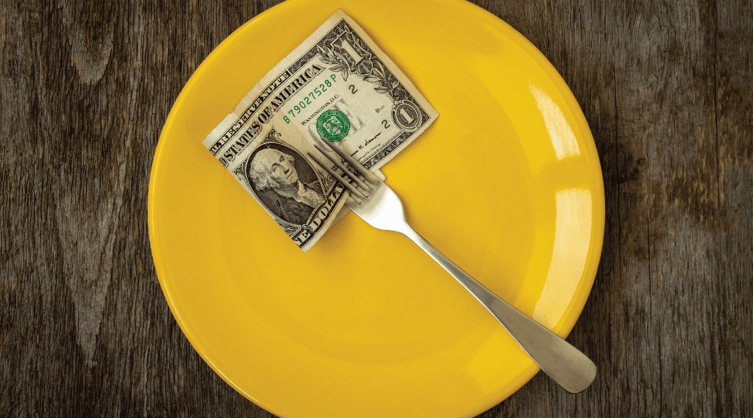 a dollar bill in the prong of a silver fork on a yellow plate