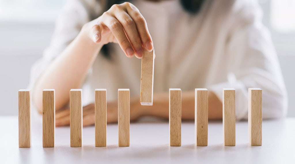 close up of a hand removing one domino block from a line of dominos blocks.