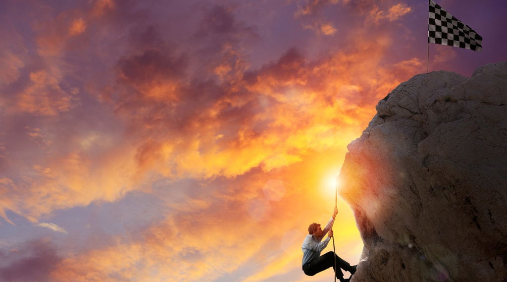 a person holding on a rope to climb up a rock and get to the finish flag.