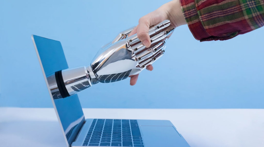 a robotic hand reaching out of a laptop screen shaking a human hand.