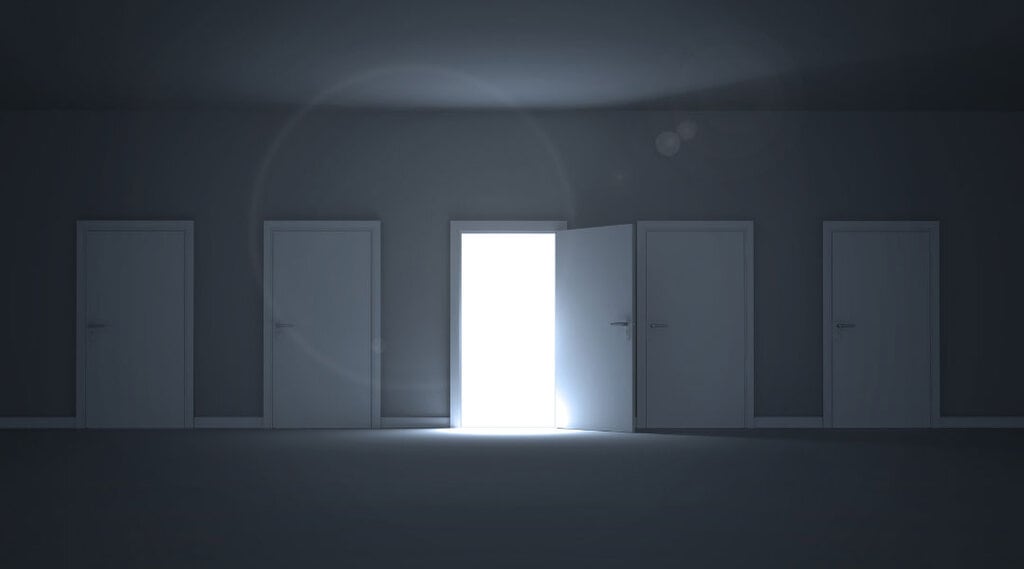 a dark room with four closed doors and one open door with a lit up doorway