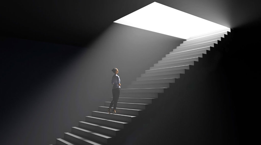 Person ascending a staircase from a dark area to a lit up entry way.