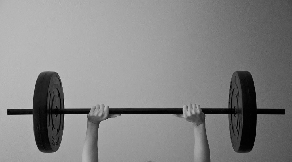 a persons hands pushing a barbell Up With Weights on both sides.