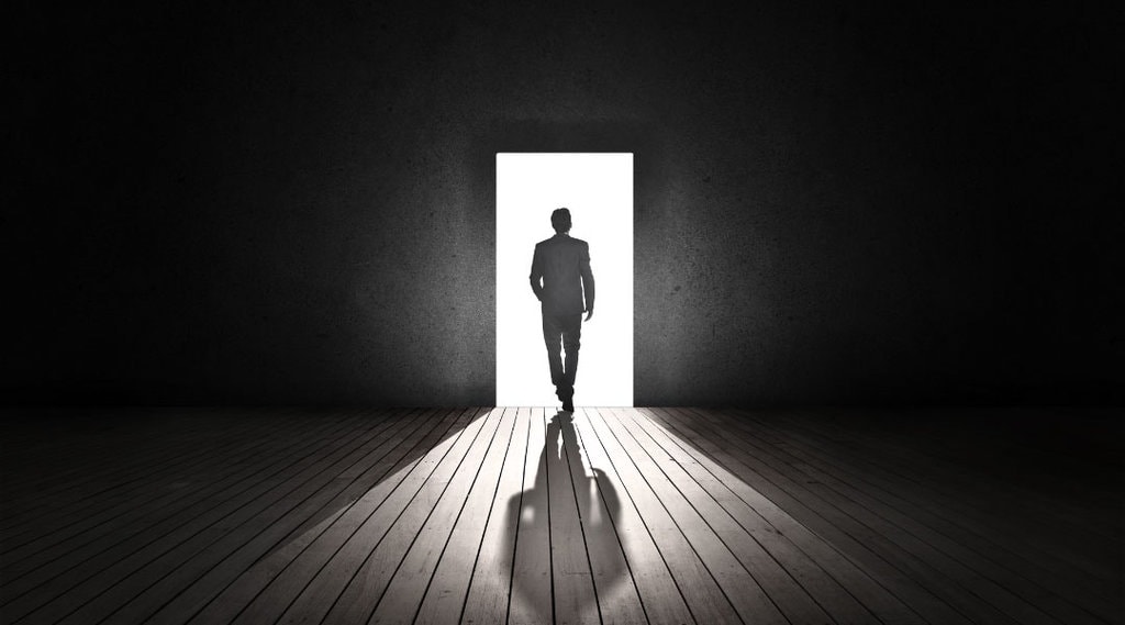 a person leaving a dark room, walking into a lit up doorway.