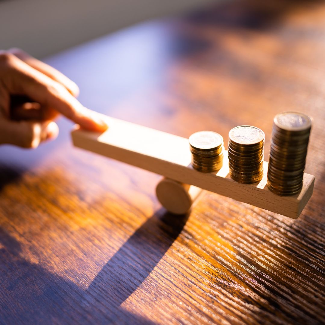 person holding one side of balance beam with stack of coins on other side