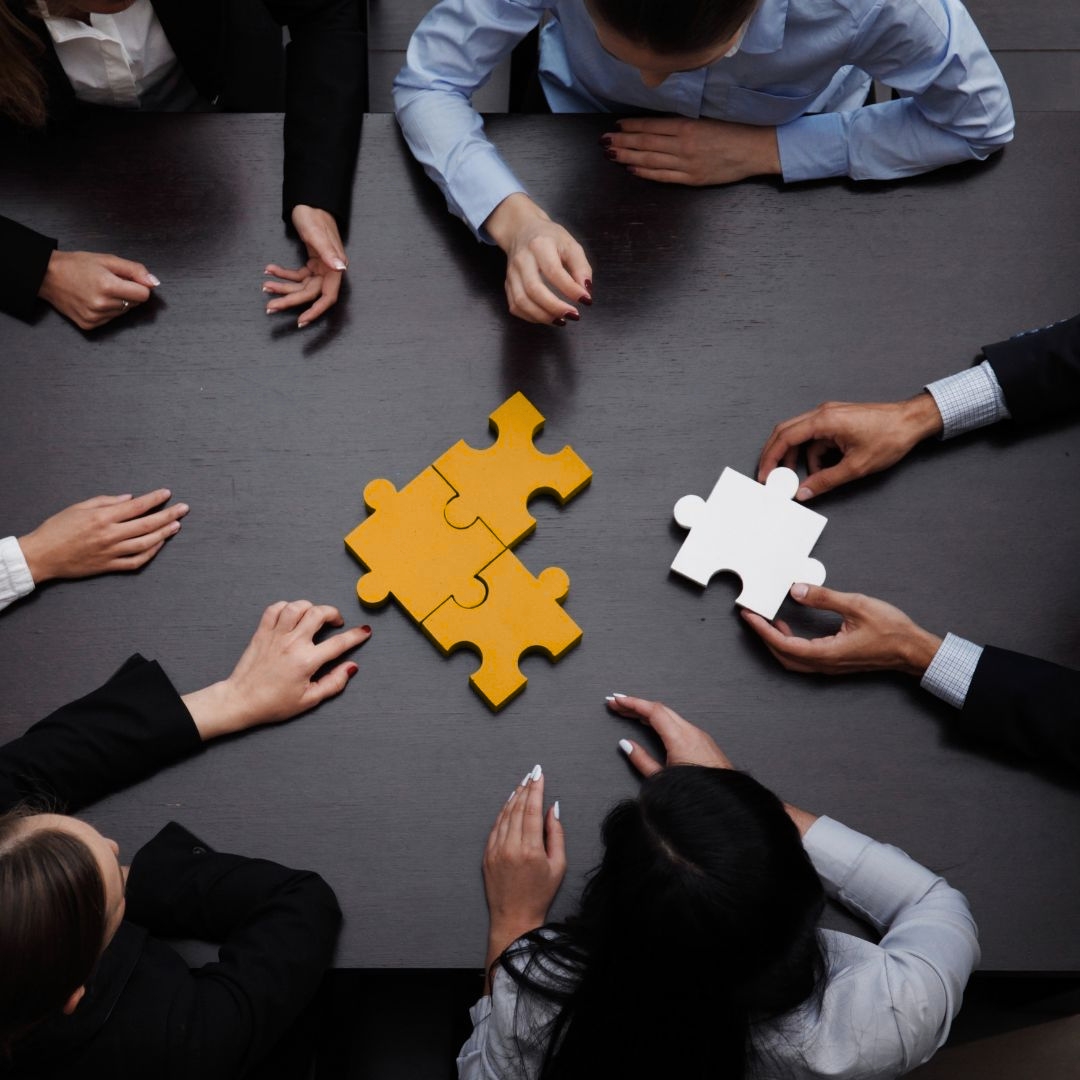 Office Workers Around a Desk Putting a Puzzle Piece Together