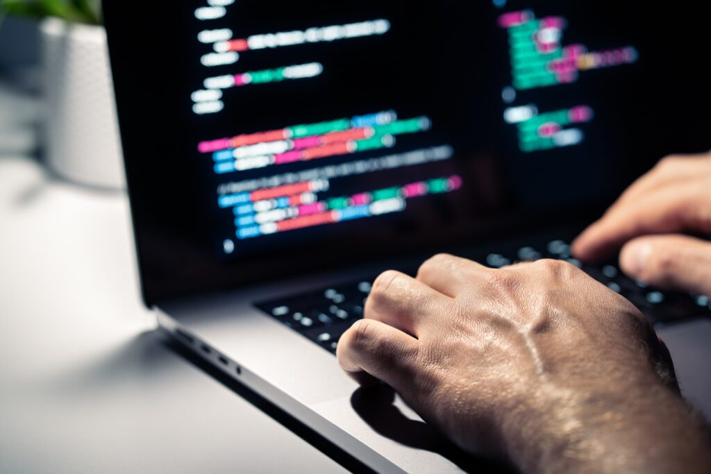 close up of someone typing on a laptop that is displaying coding. 