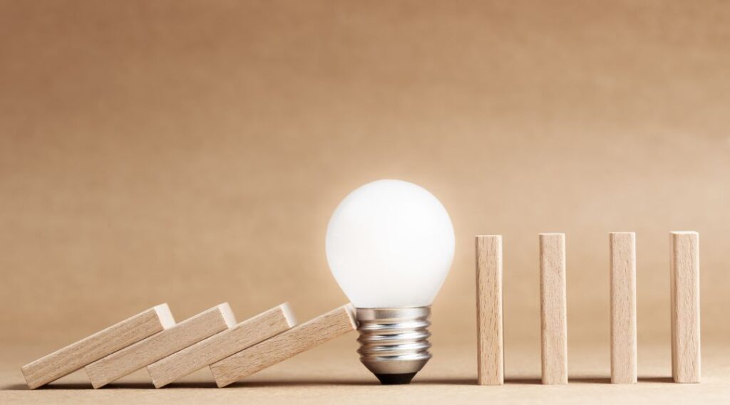 Light bulb preventing wooden dominoes from falling, symbolizing proactive problem solving