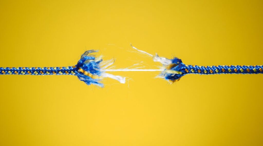 Close-up of a blue and yellow rope beginning to snap and fray against a solid yellow background, symbolizing weakness or breaking point.