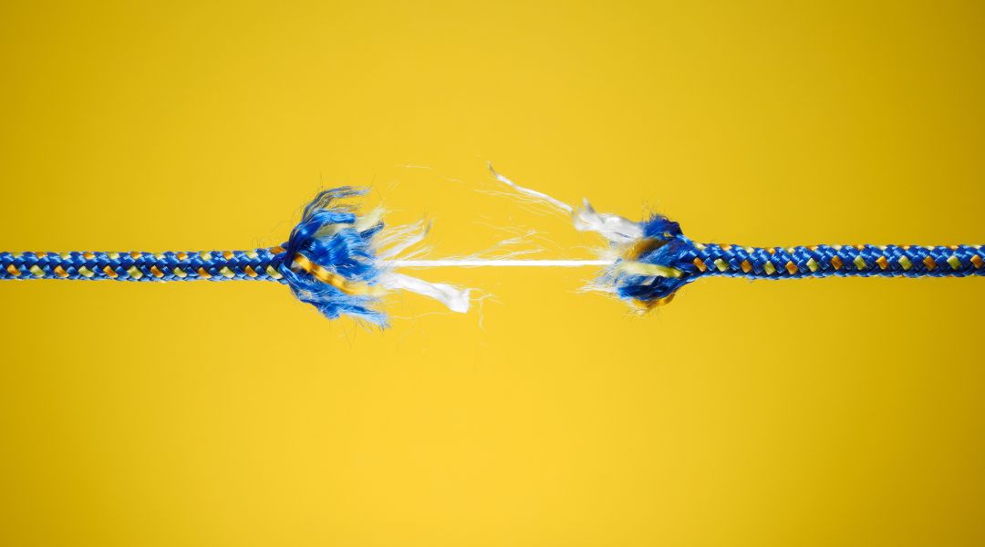 Close-up of a blue and yellow rope beginning to snap and fray against a solid yellow background, symbolizing weakness or breaking point.